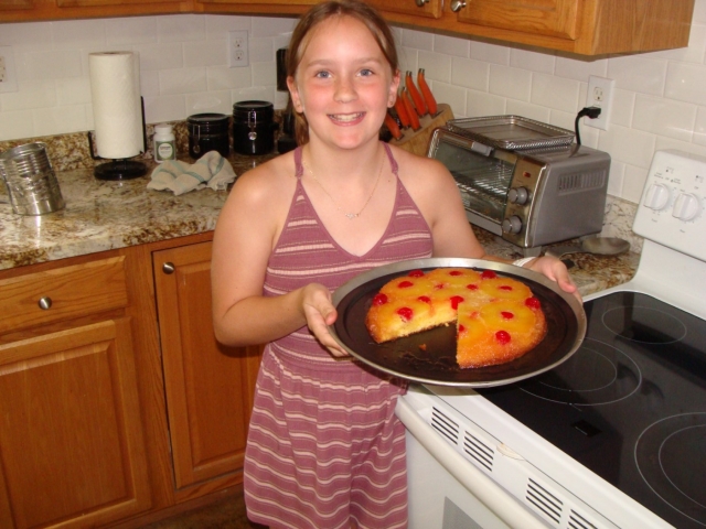 A girl holding a cake in front of a stove.