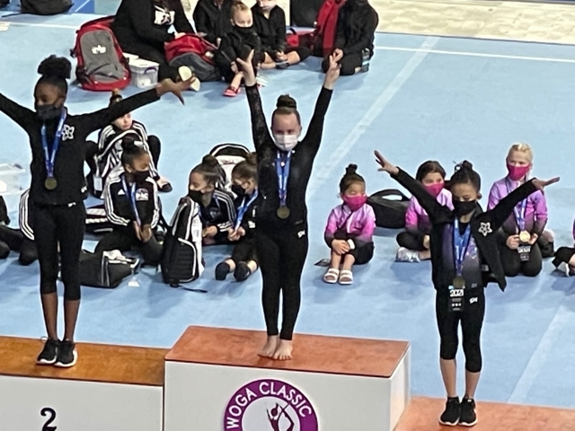 A group of gymnasts on a podium with their hands raised.