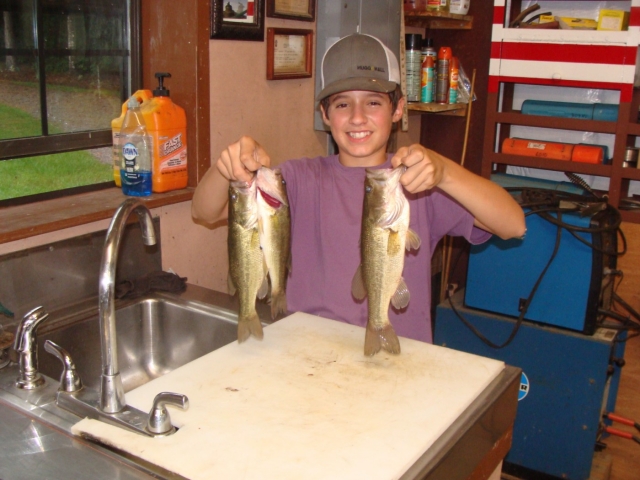 A boy holding two fish in front of a sink.