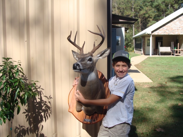 A young boy holding a deer head in front of a house.