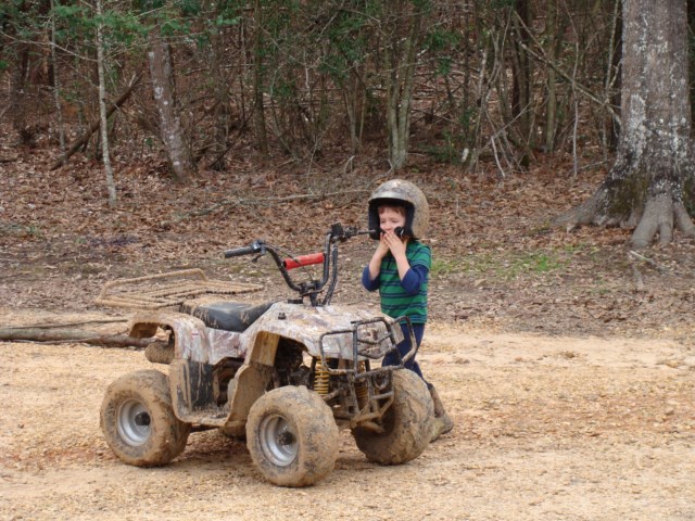 A young boy riding a four wheeler in the woods.