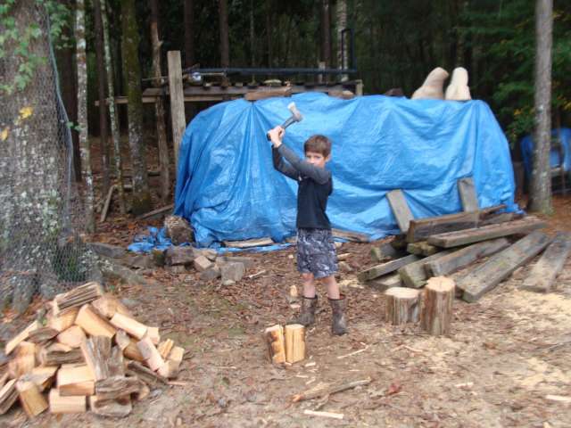 A boy with a hammer in front of a tarp in the woods.