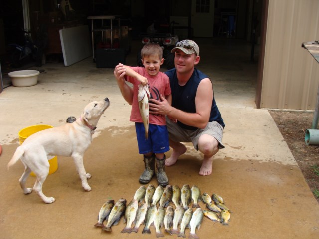 A man and a boy standing next to a pile of fish.