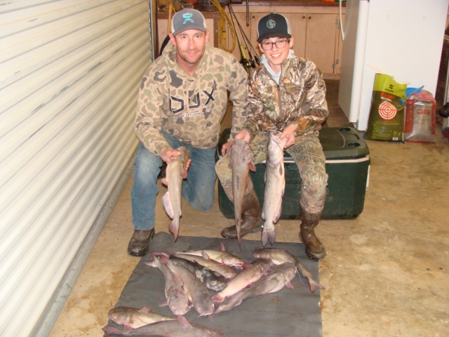 Two men posing with fish in a garage.