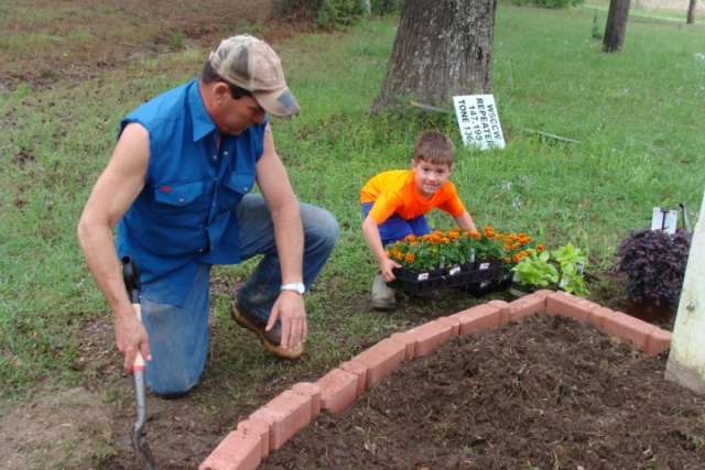 A man and a boy planting flowers in a garden.