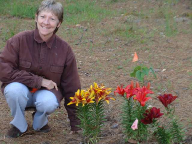 A woman kneeling down next to a flower bed.