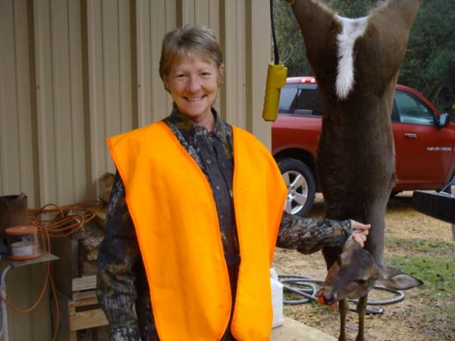 A woman holding a deer in an orange vest.