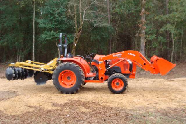 An orange tractor parked in the woods.