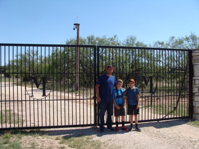 A man and two boys standing in front of an iron gate.