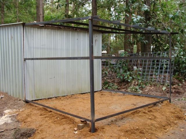 A chicken coop in the woods with a metal frame.