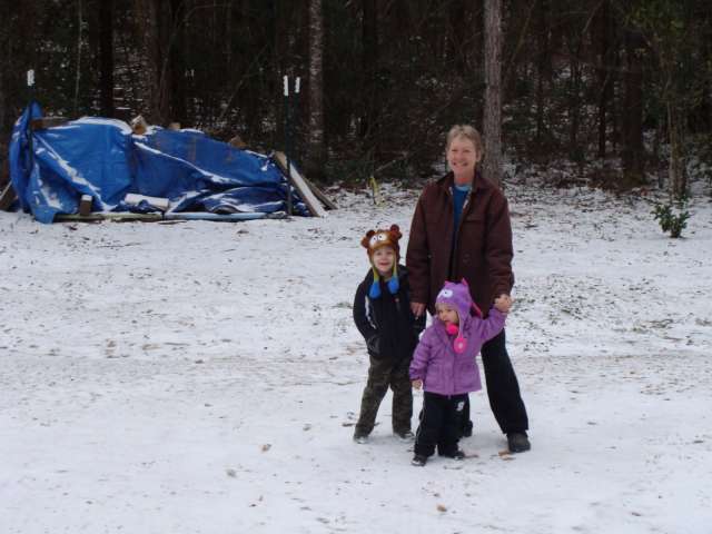 A woman and two children standing in the snow in front of a tent.