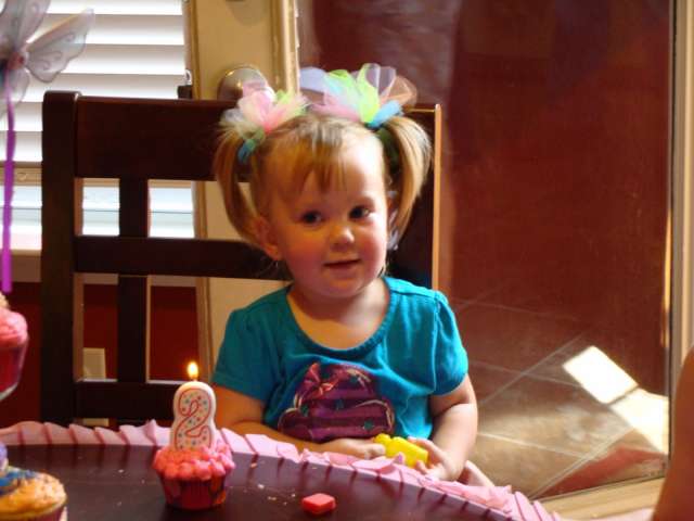 A little girl sitting at a table with a birthday cake.