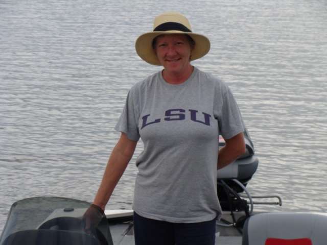 A woman wearing a hat and a lsu t - shirt standing on a boat.