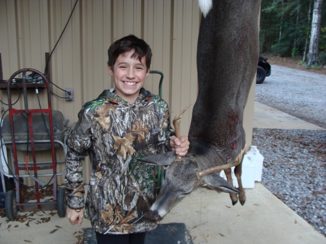 A young boy holding a deer in front of a garage.