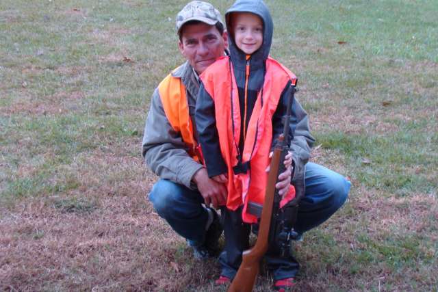 A man and a young boy posing with a rifle.