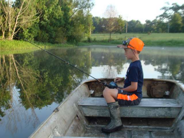 A boy in an orange hat is fishing in a small boat.