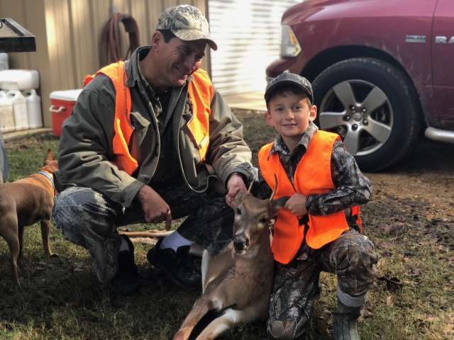 A man and a boy posing with a deer.