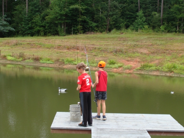 Two boys fishing on a dock in a pond.